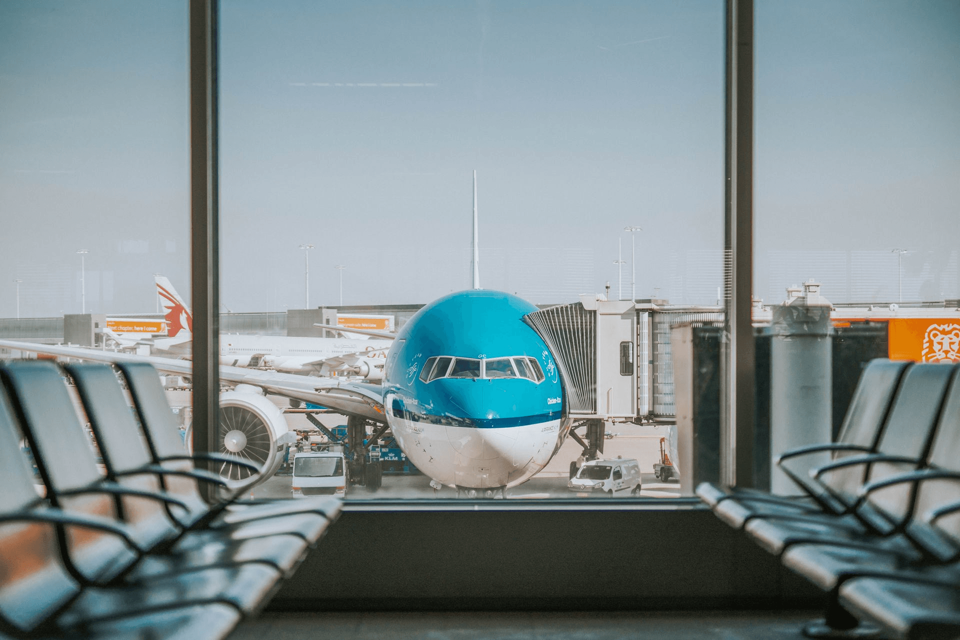 View of an airplane parked at an airport gate, seen from inside of a terminal with rows of empty seats
