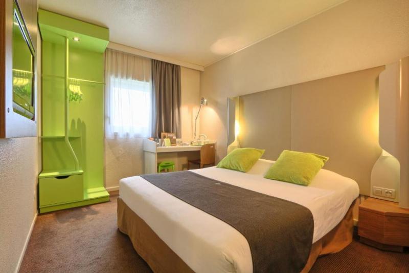An accessible guest room with a carpeted floor, a double bed, a desk, an open closet and a wall-mounted TV.