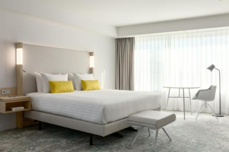 An accessible guest room with a carpeted floor, a double bed, a table and a chair and large windows