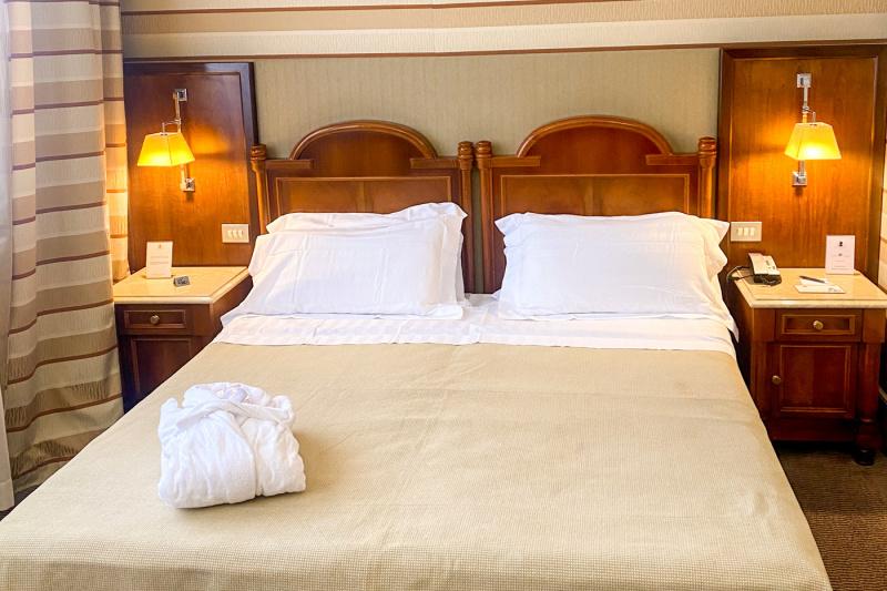 This superior room has two single beds that can be pushed together. There are nightstands on the outside of each bed. On one nightstand there is a telephone with a notepad and pen. Reading lamps are mounted above each nightstand.