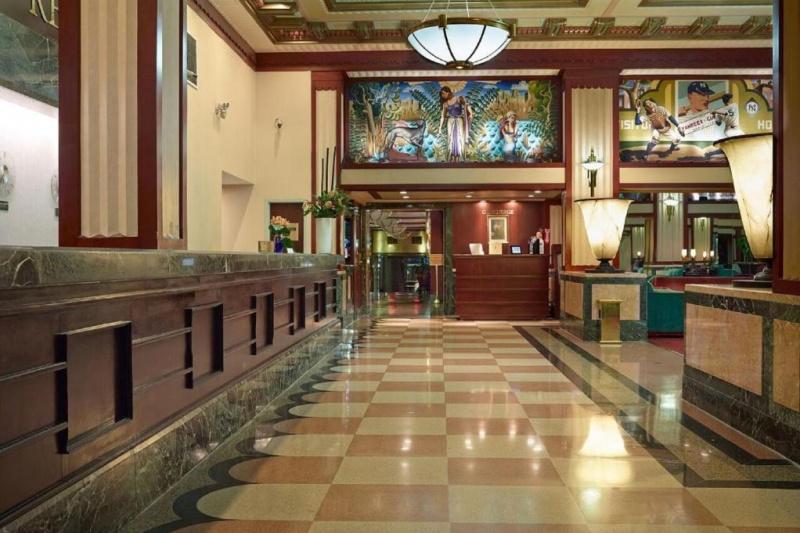 The hotel lobby has a marble floor, wood paneling, art deco lamps and artwork on the walls.