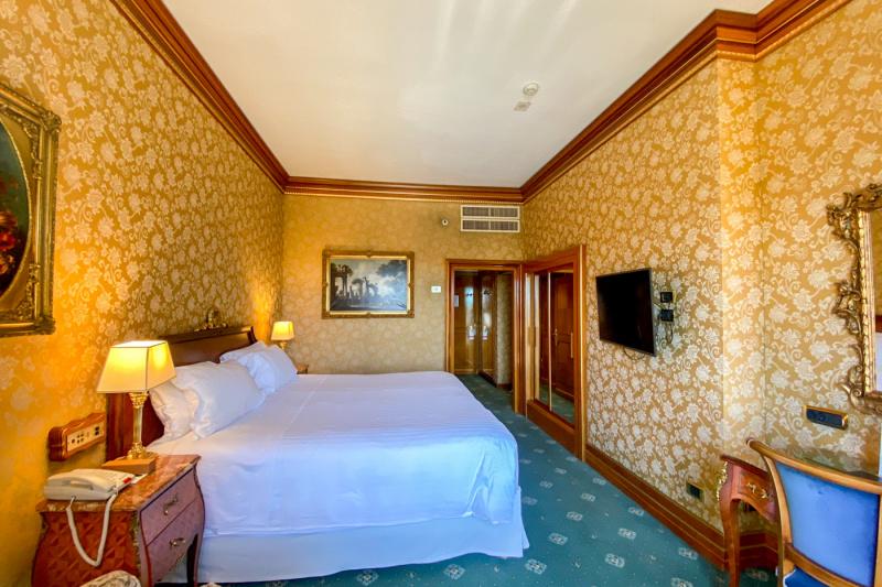 The Superior double room has a large double bed with a telephone next to the bed, a full-length mirror and artwork on the walls.