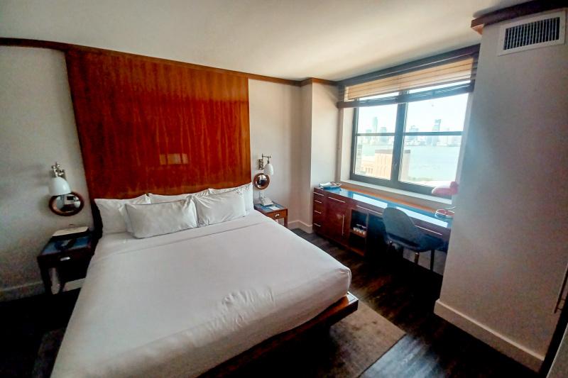 The superior king room has a king-size bed with lamps on either side. There is a desk under a window on one side. The desk has a reading lamp, a chair underneath and built in cupboards to one side.