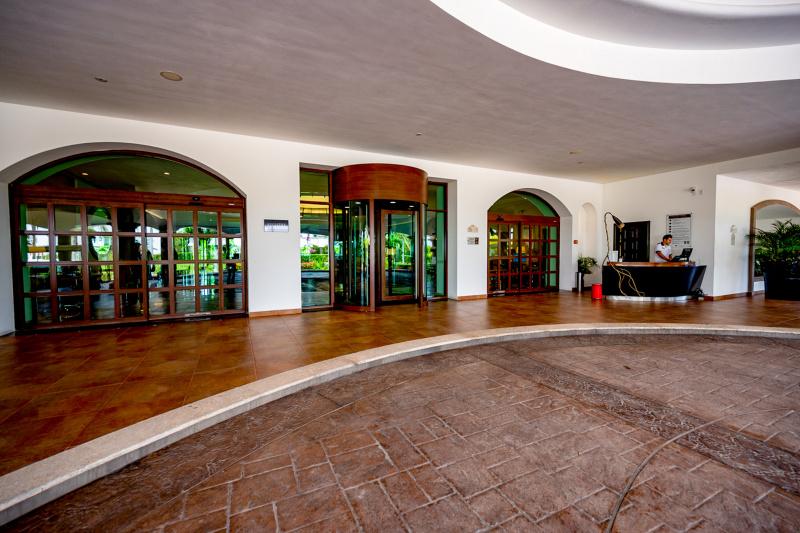 The hotel entrance has a large drive-up area with a small curb leading up to a revolving door. There are also automatic sliding glass doors and a reception desk to one side of the doors.