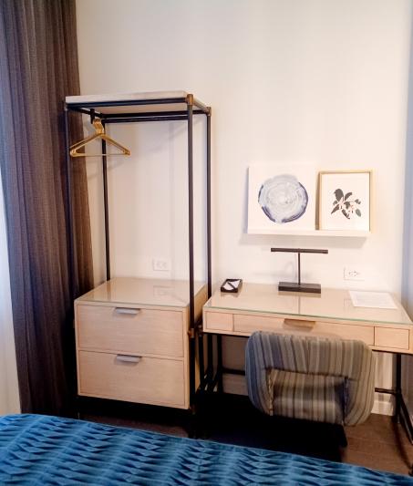 In the room, opposite the bed, there is a workstation and movable chair. Between it and the window there is a shelf unit with 2 drawers and a high clothes rail.