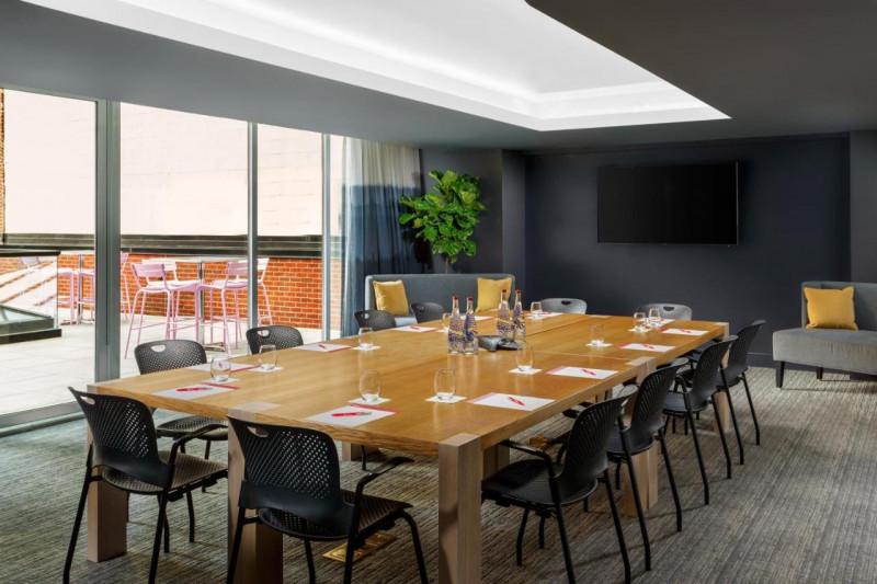 The spacious conference room has a 12 seater table. There is a wall-mounted TV and 2 sofas. There are french doors leading to an outdoor seating area.