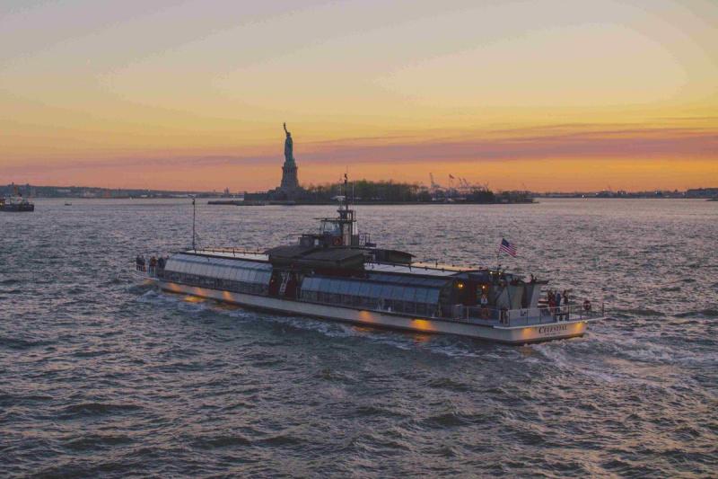The cruise boat sets sail towards the Statue of Liberty, with the sun setting in the background.
