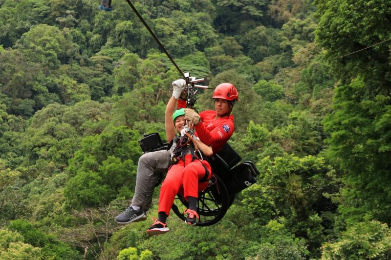 A traveler is zip lining with a professional guide and her wheelchair.