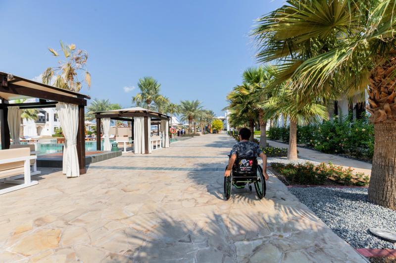 A guest uses a wheelchair to navigate the hotel swimming pool area and cobblestone patio