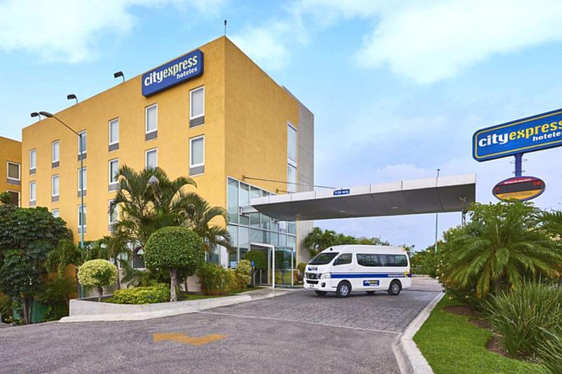 Experior view of City Express Tuxtla Gutiérrez hotel with a drop off area, hotel shuttle, and step free entrance.