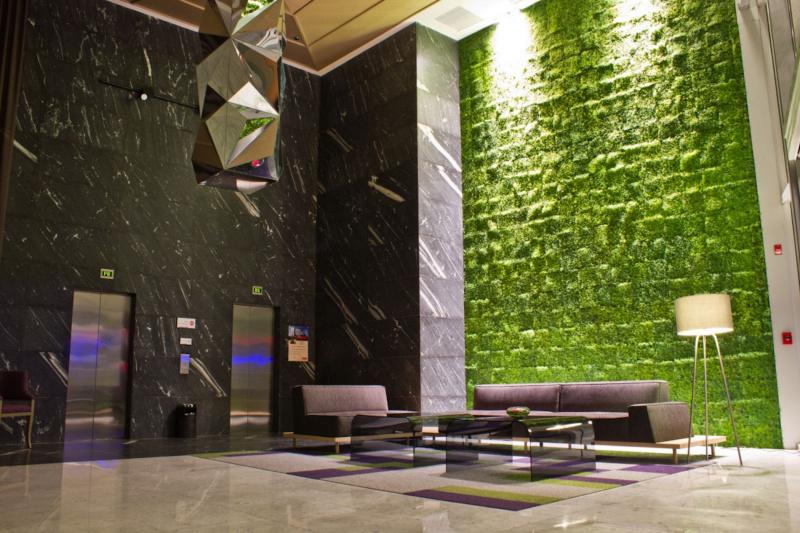 Spacious lobby with two elevators, high ceilings, a plant wall, and a sleek seating area