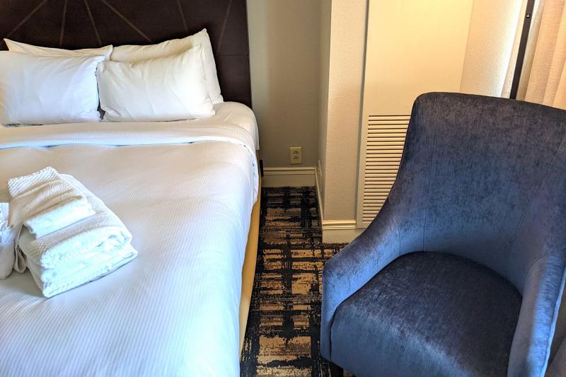 An accessible guest room with 2 queen-sized beds, an armchair and a carpeted floor.