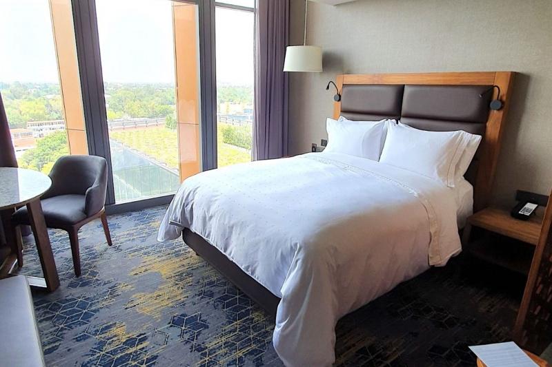 A guest room at the hotel, with a king-sized double bed, floor-to-ceiling windows, a bedside table, a table and chair and a carpeted floor.