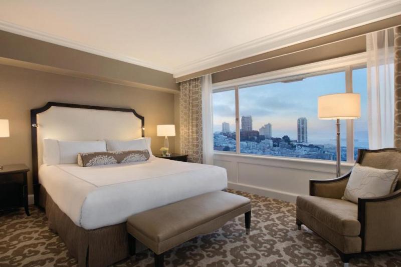An accessible guest room with a double bed, a carpeted floor, an armchair and a city view.