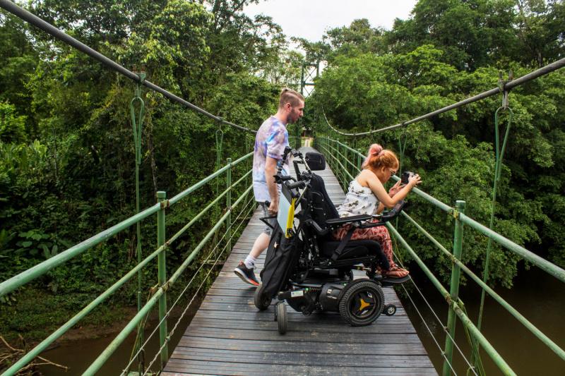 Wheel the World traveler and companion cross a rainforest bridge
