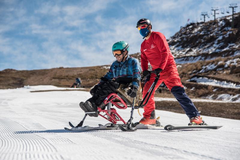 An instructor pushed a skiier sitting on adaptive equipment.