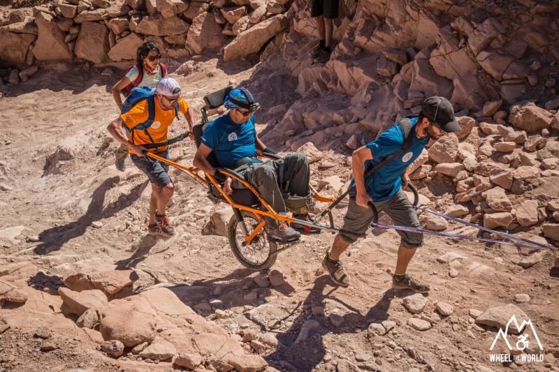 A group of friends travers desert uneven lands using a joëlette wheelchair