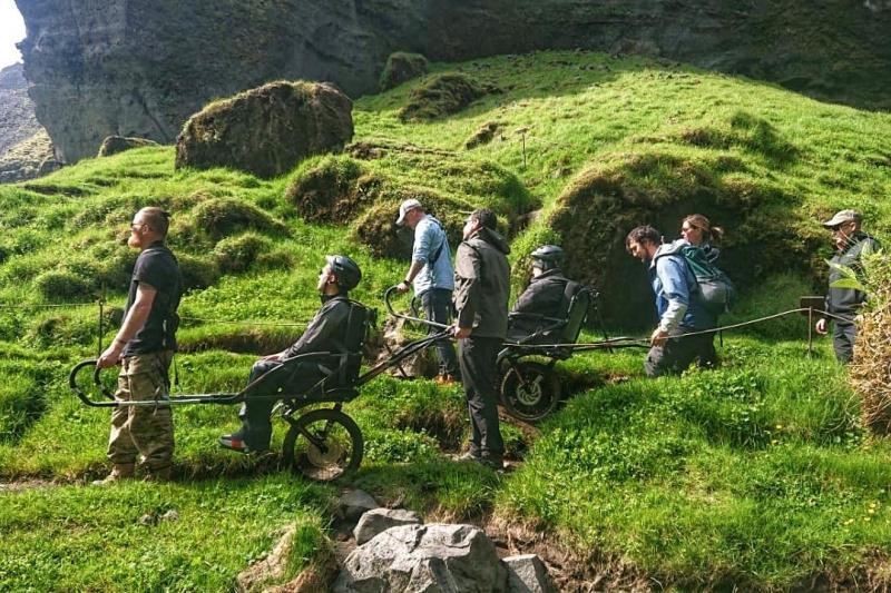 A group of friends travers uneven lands using a joëlette wheelchair