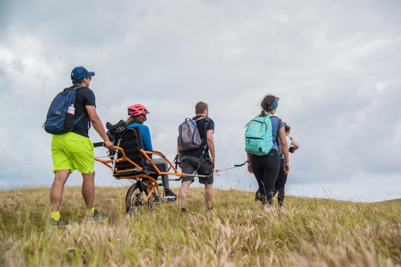 A group of friends travers uneven Easter Island lands using a joëlette wheelchair