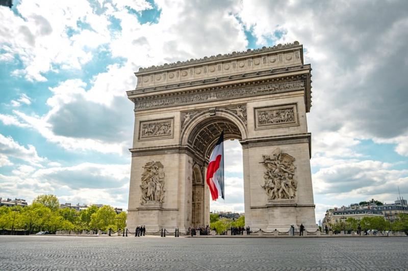 The Arc de Triomphe, with a French flag hanging in the middle of the arch.